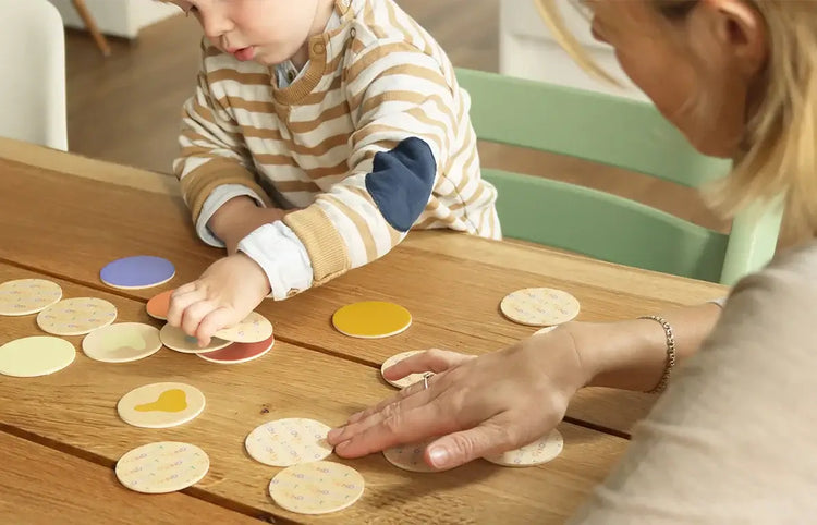 Kind spielt Memory-Spiel aus Holz mit Erwachsenem am Tisch