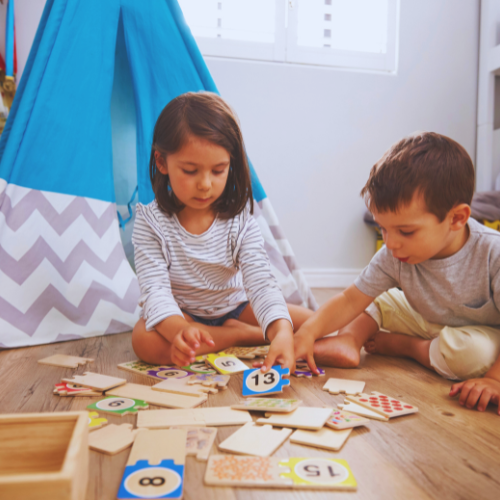 Zwei Kinder sitzen auf dem Boden und spielen gemeinsam mit einem Puzzle. 