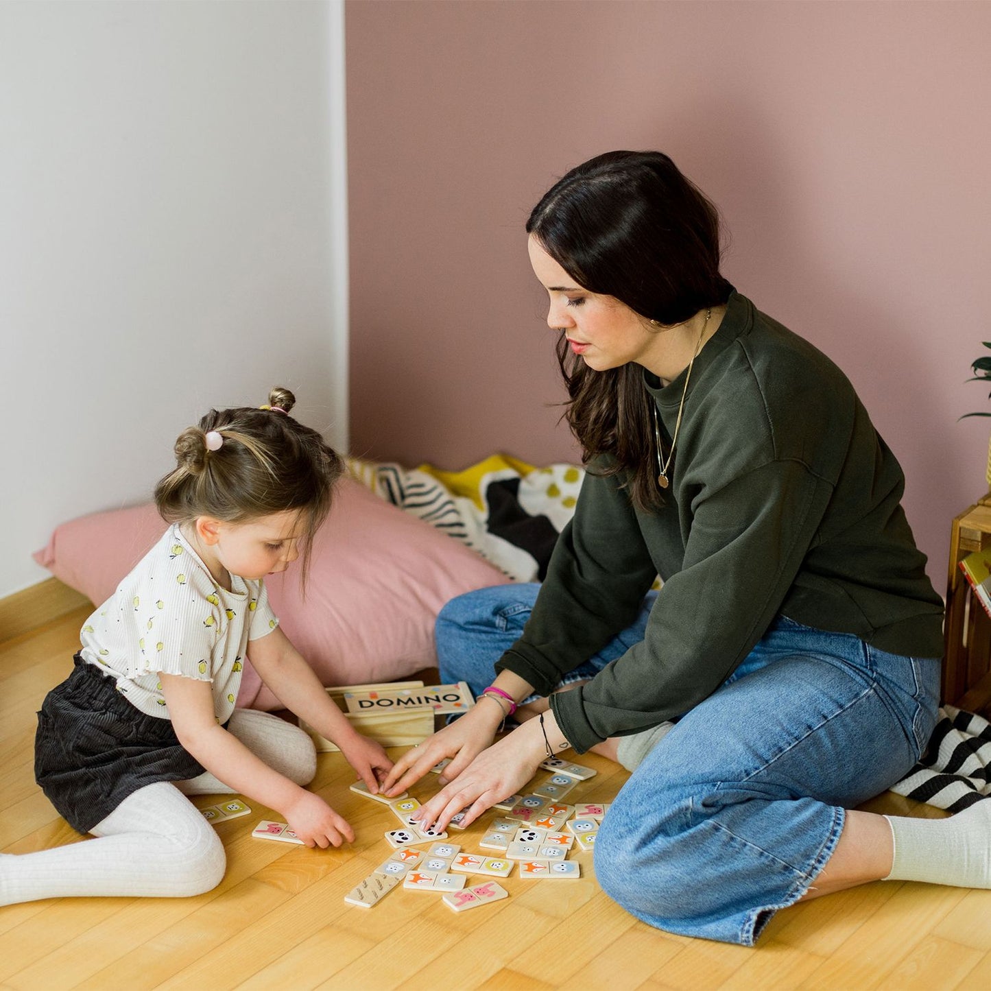 Der Raum zeigt eine rosa Wand und eine weiße Wand, während Mutter und Kind das Domino-Tier-Spiel spielen.