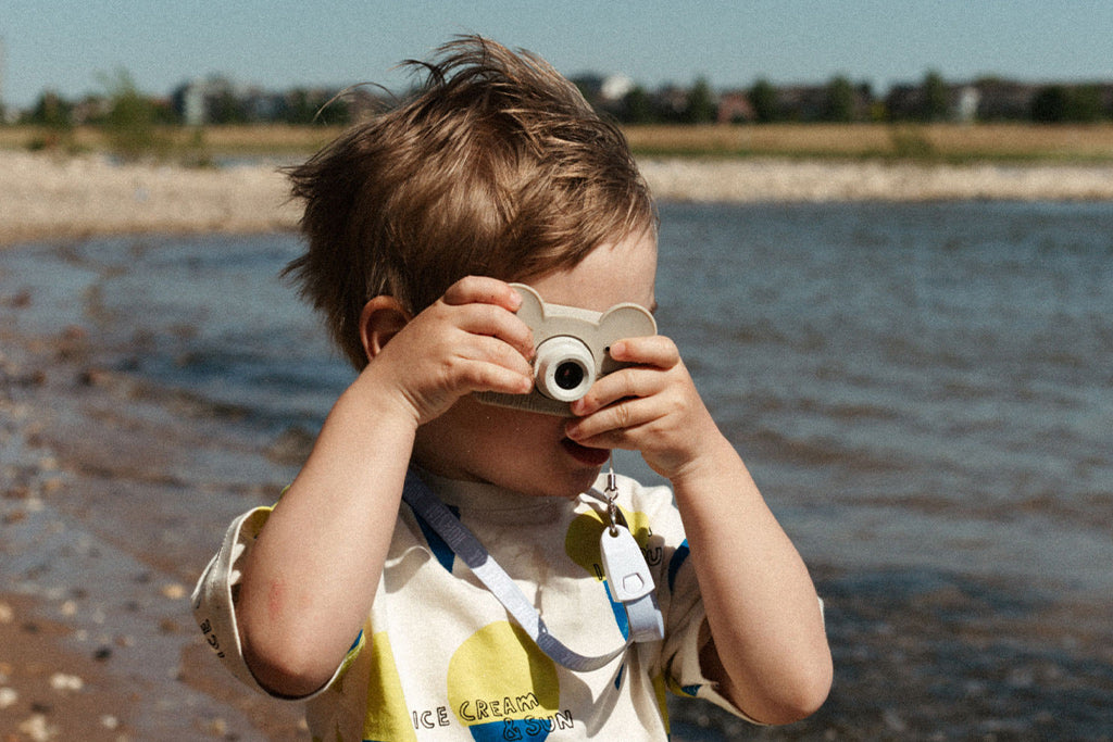 Ein Kind am Strand, das mit einer Kamera Fotos macht, während es die Umgebung erkundet und den Moment festhält.