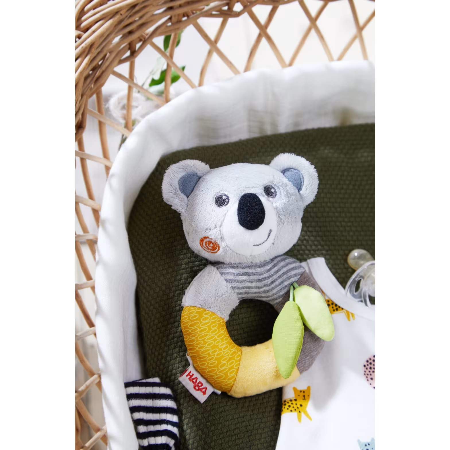 Der Greifling „Kuschel Koala“ liegt sanft im Bettchen, umgeben von Kuscheltüchern – ideal für Babys zum Schmusen und Entspannen.