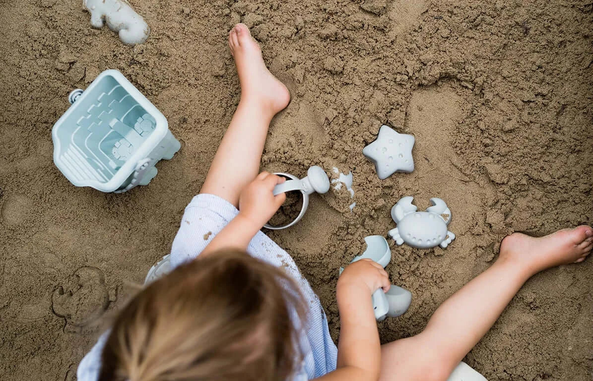 Ein Kind benutzt das Sandspielzeug Toni, um Sand zu schaufeln und eine Sandburg zu bauen.